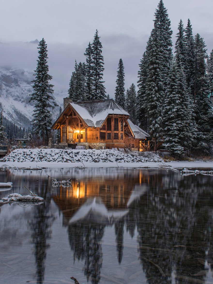 A timber lodge lit at dusk beside a still mountain lake